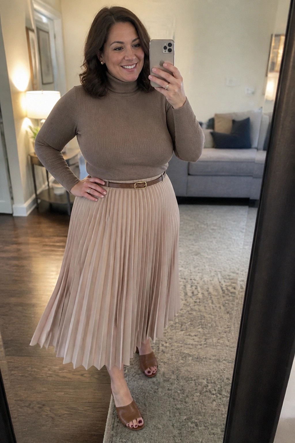 Woman in brown turtleneck and beige pleated skirt taking mirror selfie