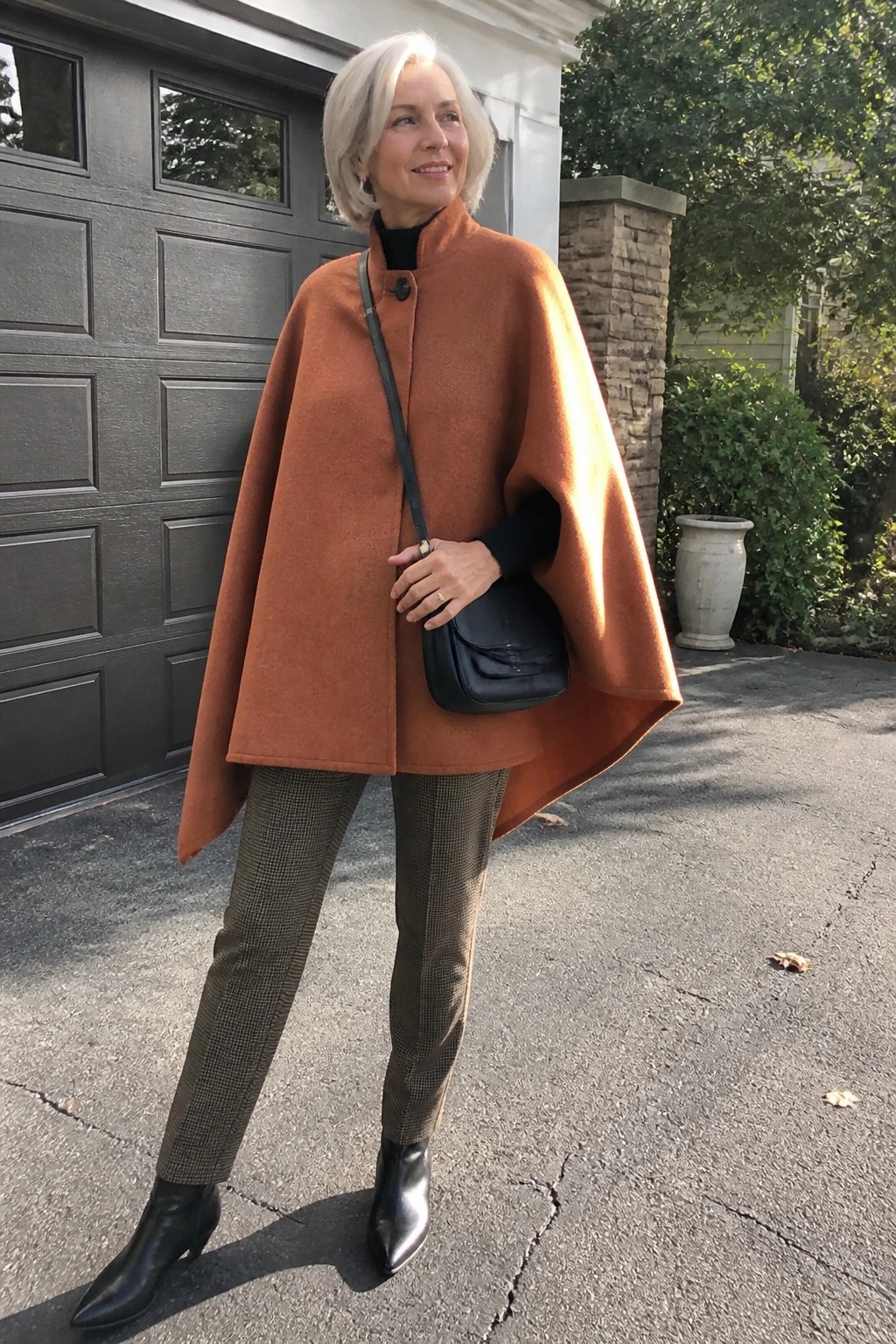 Elegant white-haired woman in rust cape coat, checkered pants, and black boots.