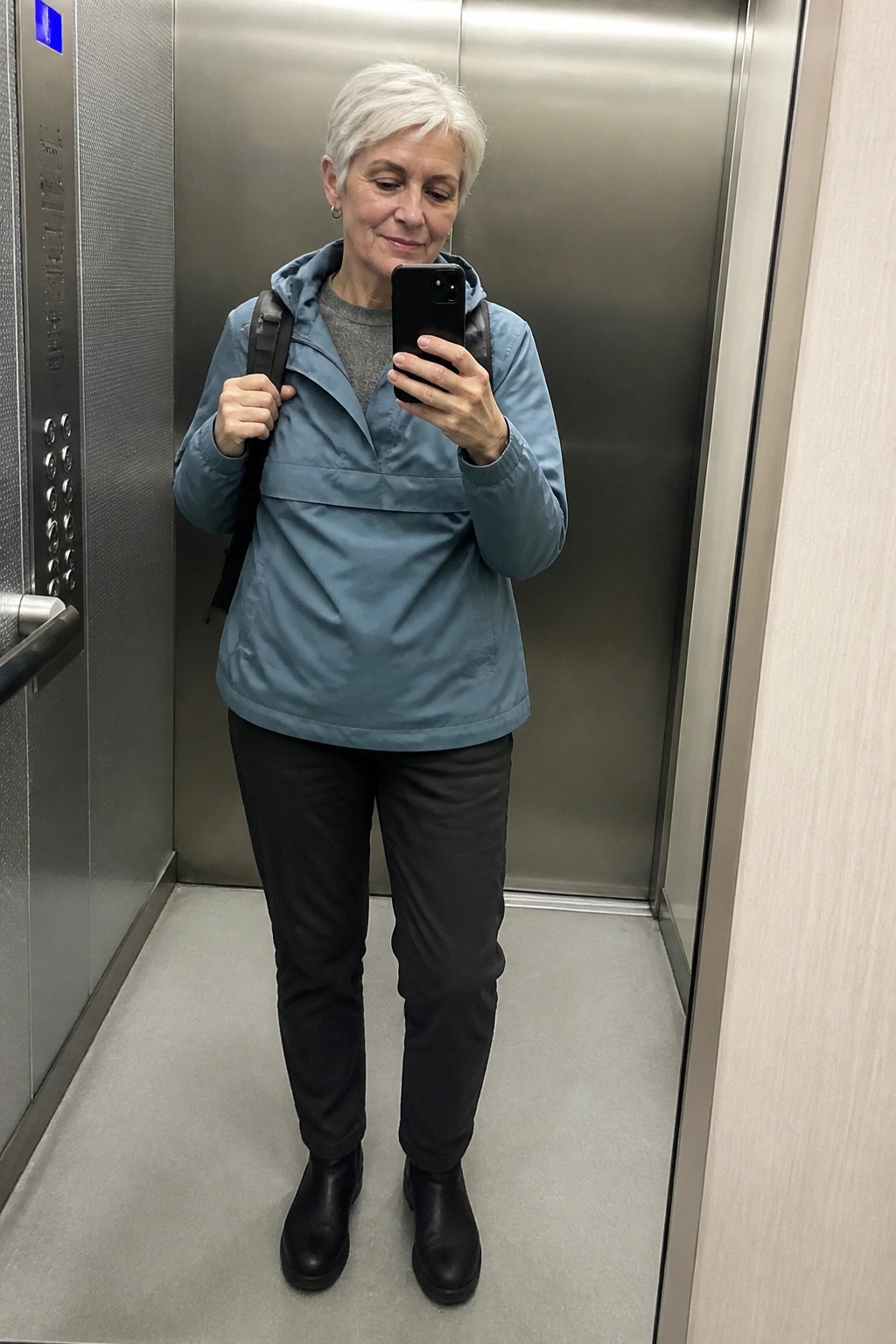 Woman with short white hair taking selfie in elevator wearing blue jacket and black pants