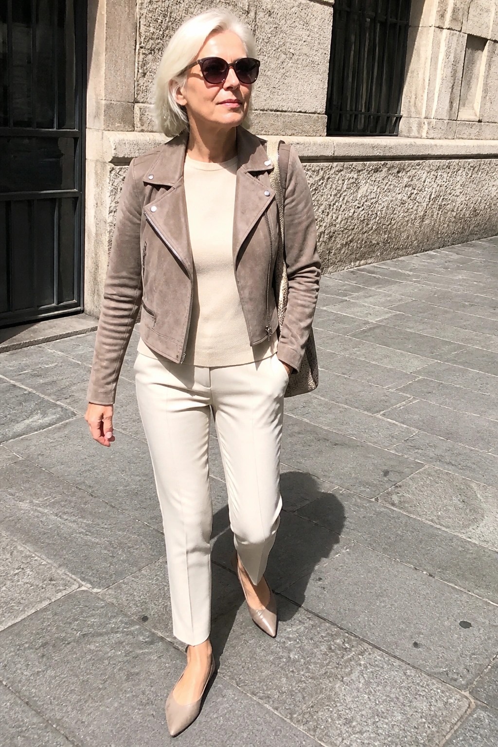 Stylish woman with white hair in taupe suede jacket and white pants on pavement