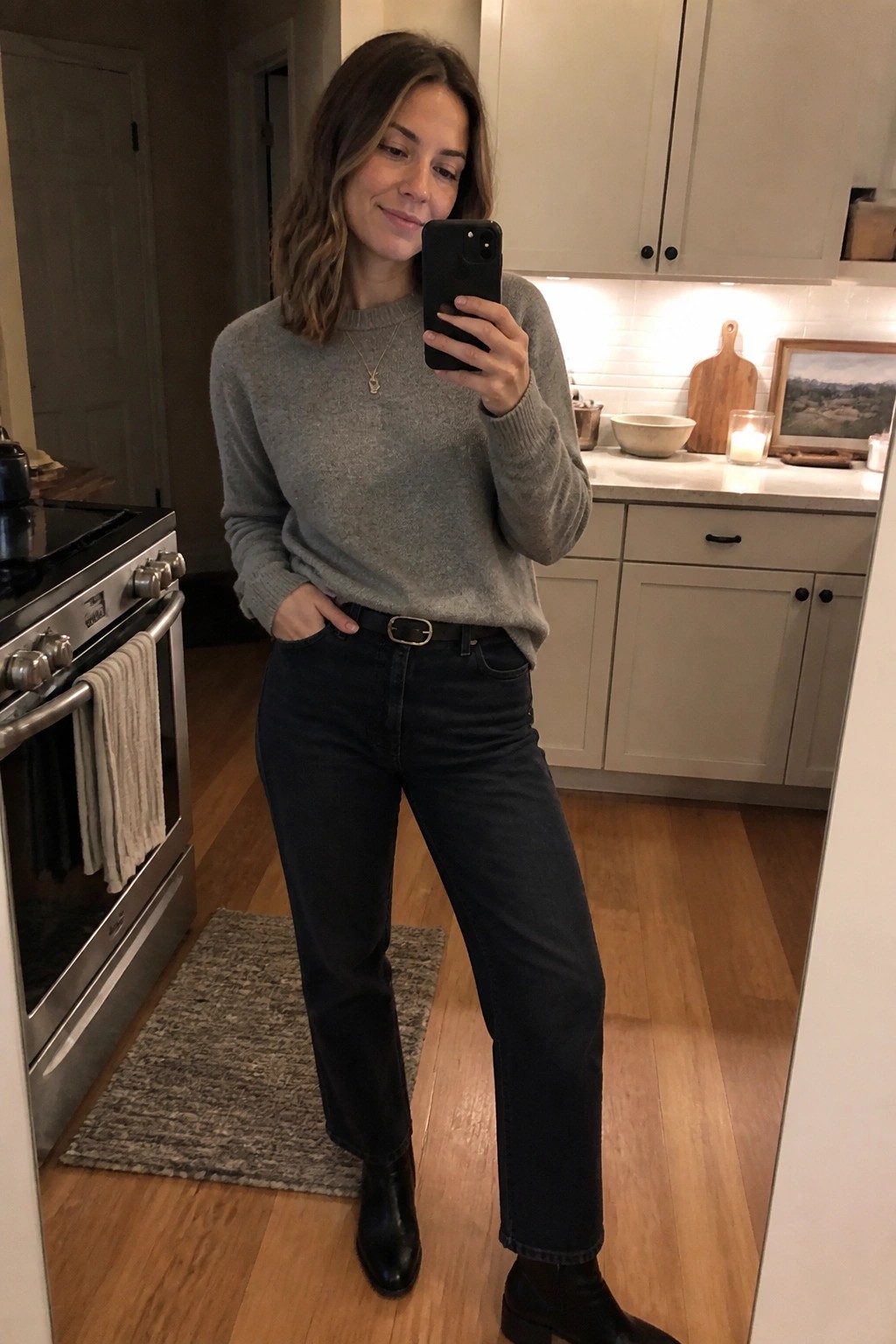 Woman in gray sweater and dark jeans taking mirror selfie in kitchen