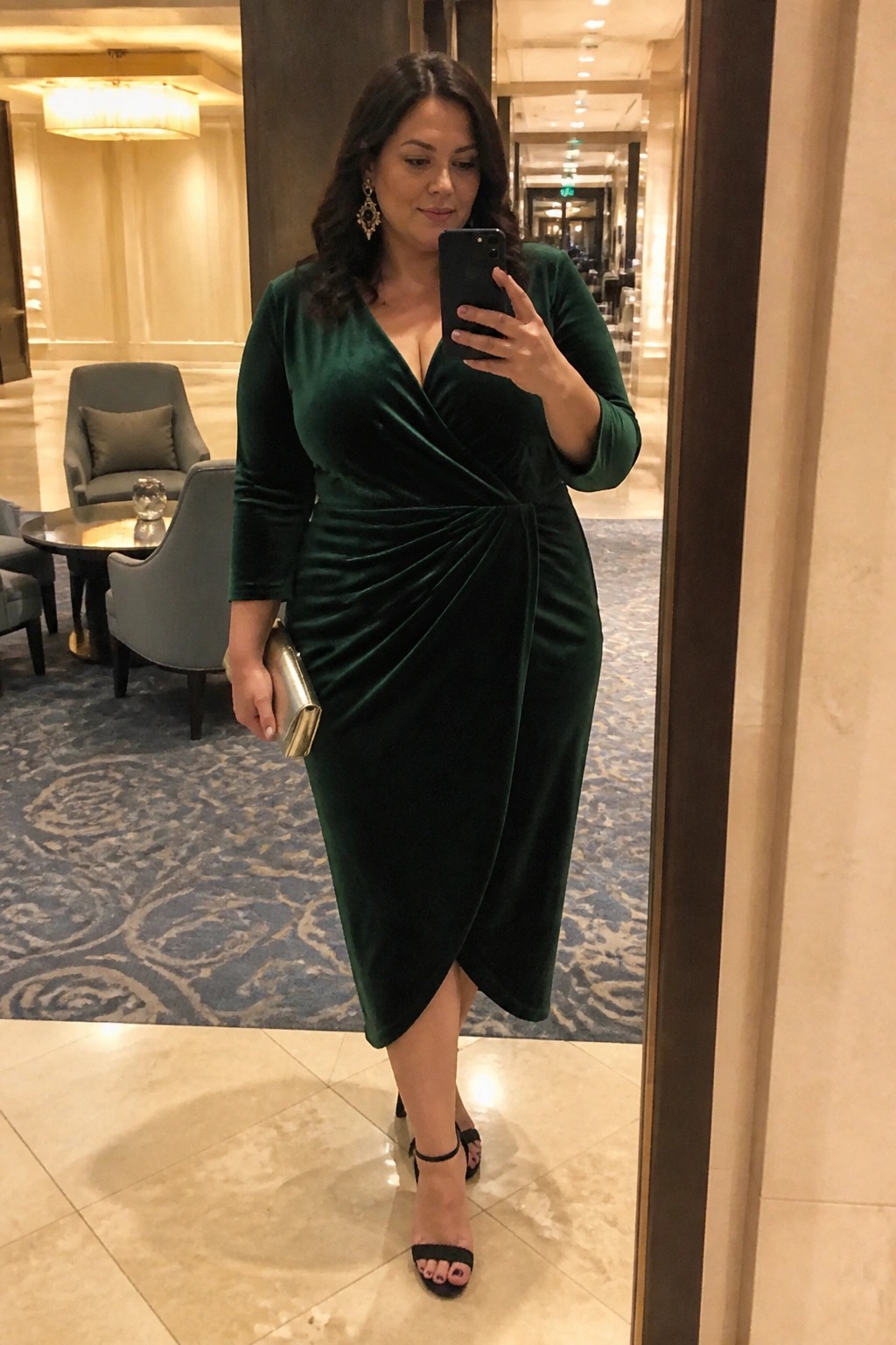 Woman in emerald green velvet wrap dress taking mirror selfie in elegant lobby