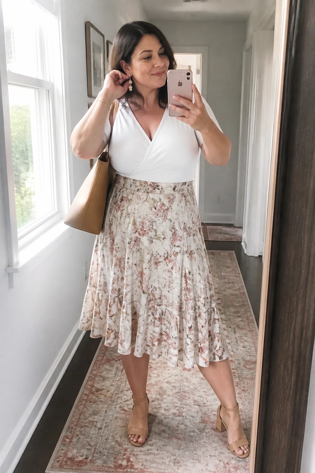 Woman in white top and floral skirt taking mirror selfie with phone and bag