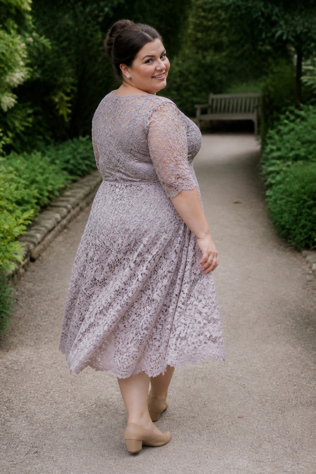 Woman in lavender lace dress smiles over shoulder on garden path