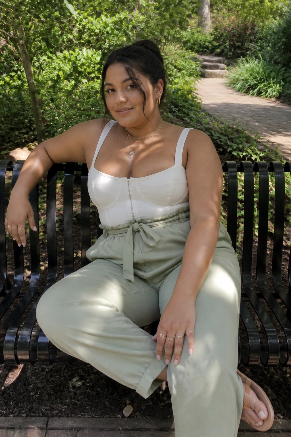 Woman in white top and green pants seated on black park bench outdoors
