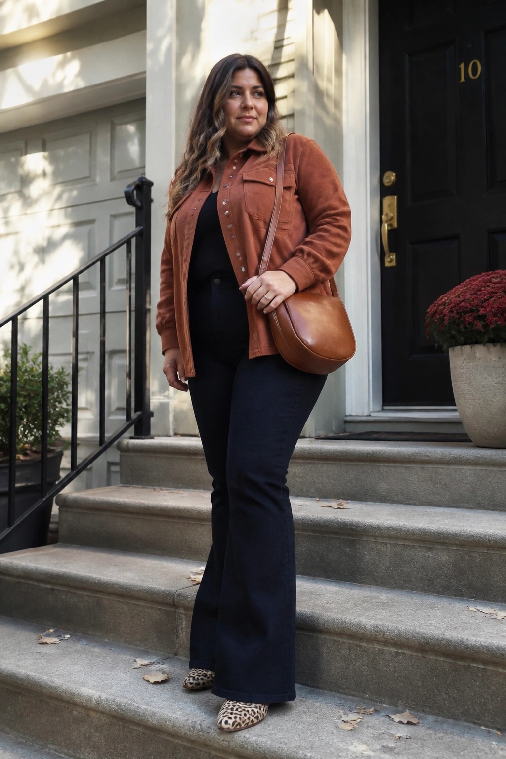 Woman in rust suede jacket and flared jeans on stone steps with brown bag