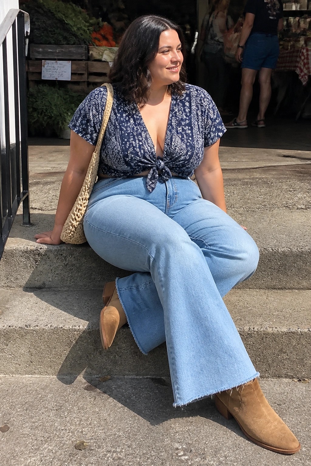Woman in blue floral crop top and wide-leg jeans on market steps with woven bag