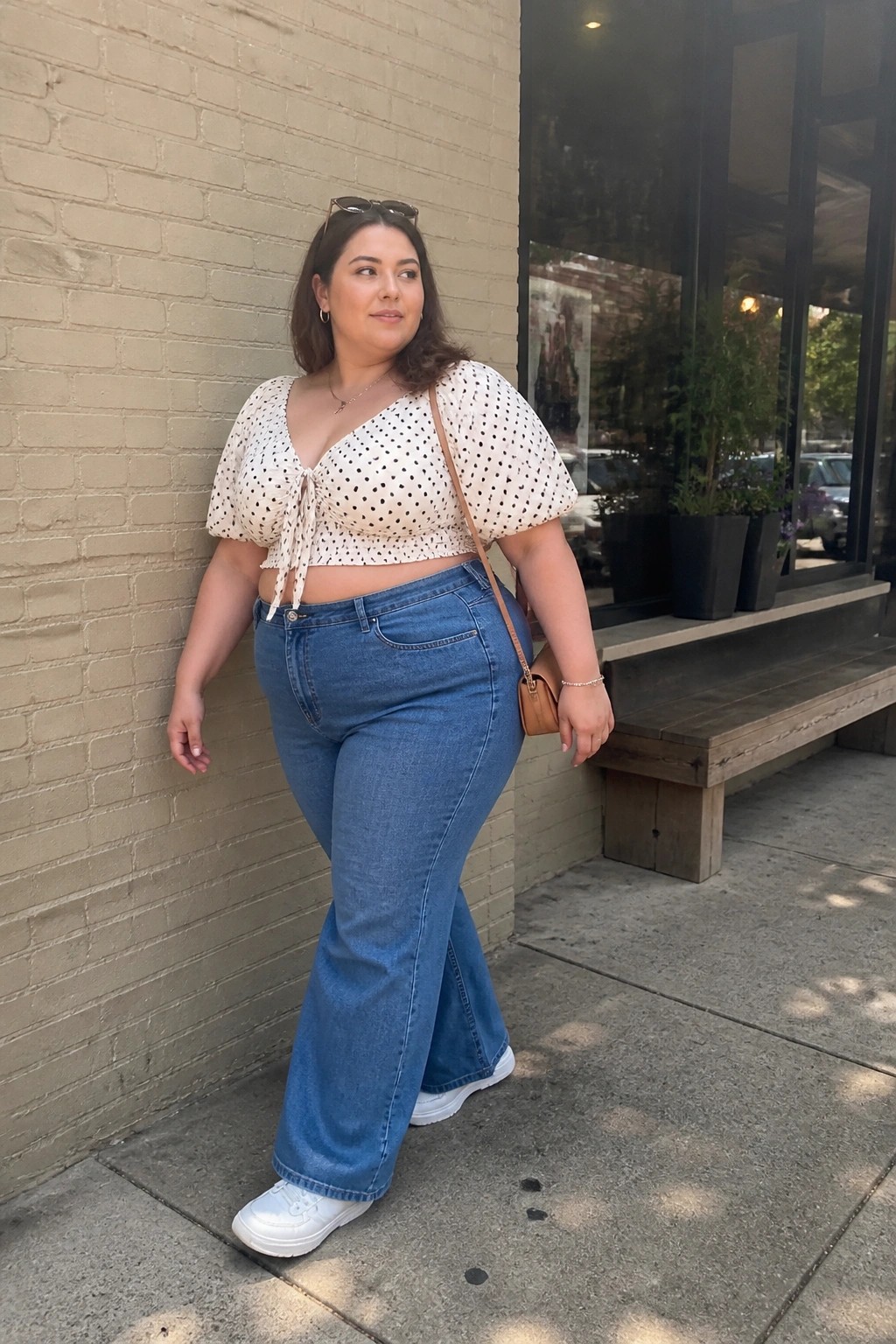 Woman in polka-dot crop top and blue wide-leg jeans against brick wall
