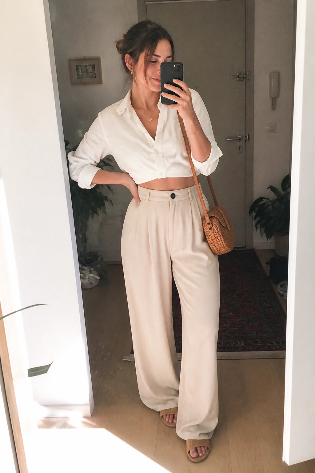 Woman taking mirror selfie in white cropped shirt and beige wide-leg pants.