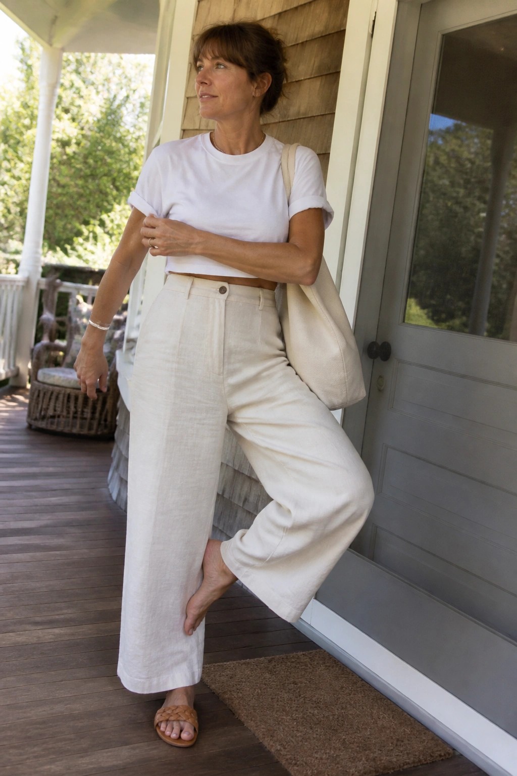 Woman in white crop top and beige linen pants with tote bag on porch