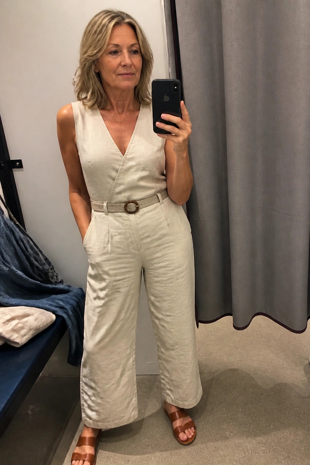 Woman in cream linen jumpsuit taking mirror selfie in fitting room