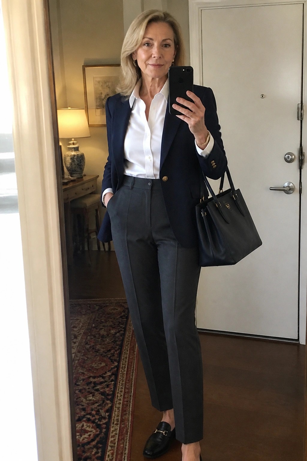 Woman in navy blazer over white button-down shirt paired with gray tailored trousers black loafers and black handbag.