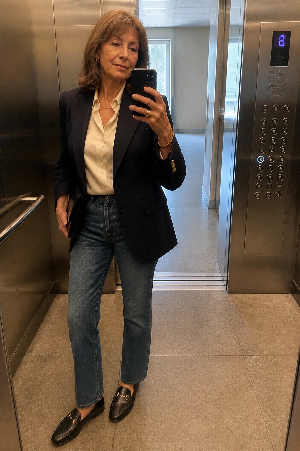 Woman in navy blazer and jeans taking phone selfie in elevator