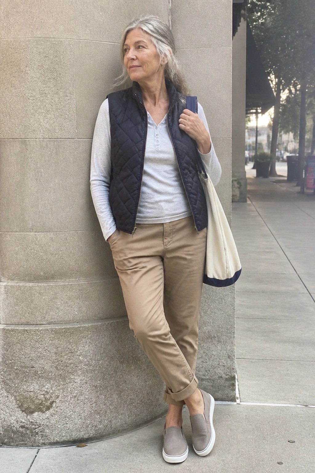 Elderly woman with gray hair in navy quilted vest and khaki pants by stone wall