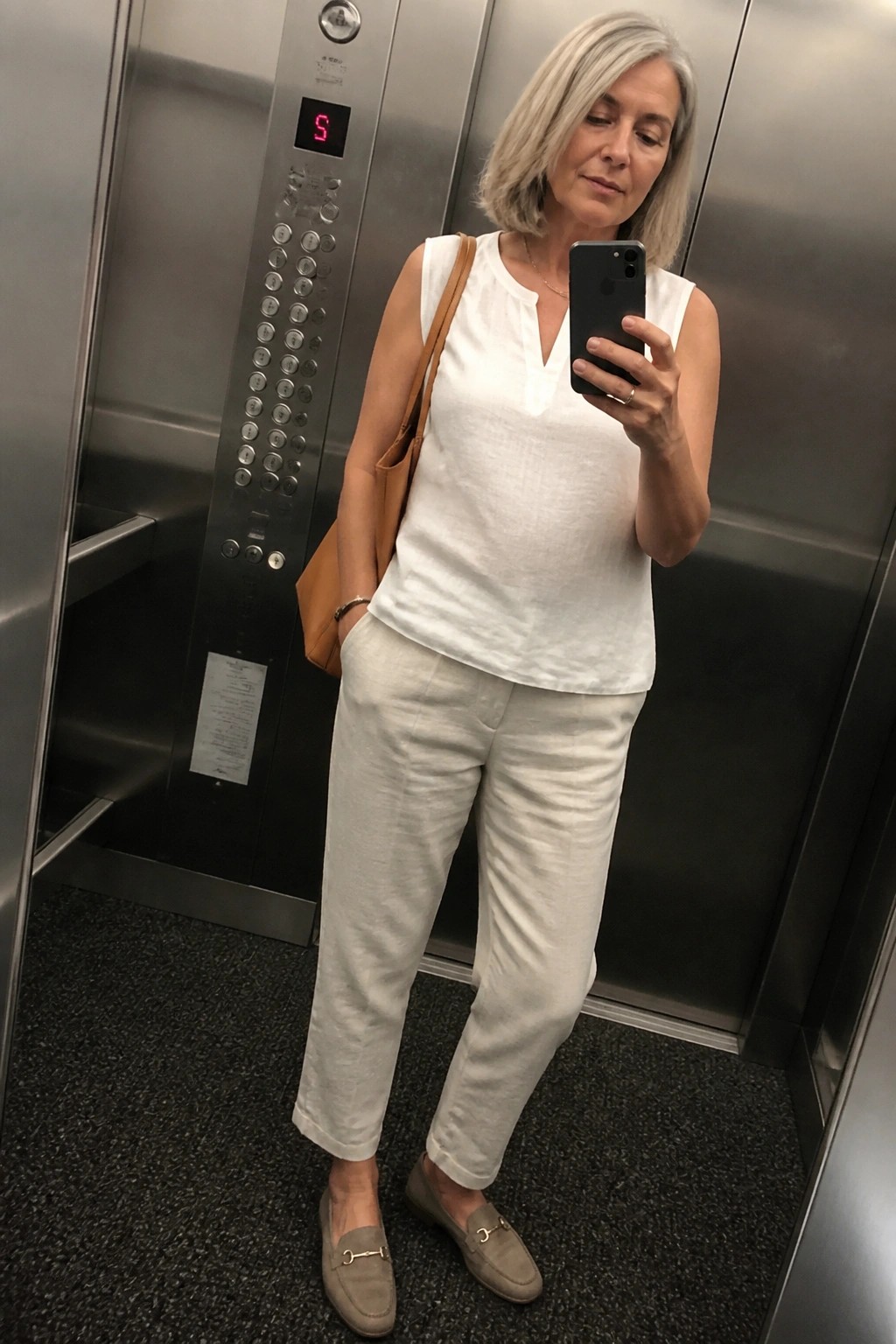 Woman with gray hair in white outfit taking selfie in elevator