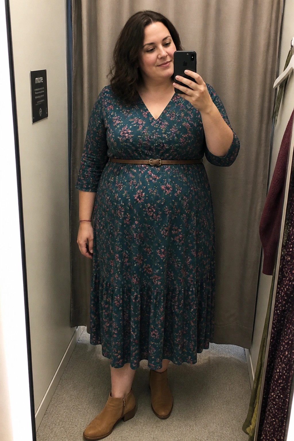 Woman in teal floral dress takes mirror selfie wearing brown ankle boots