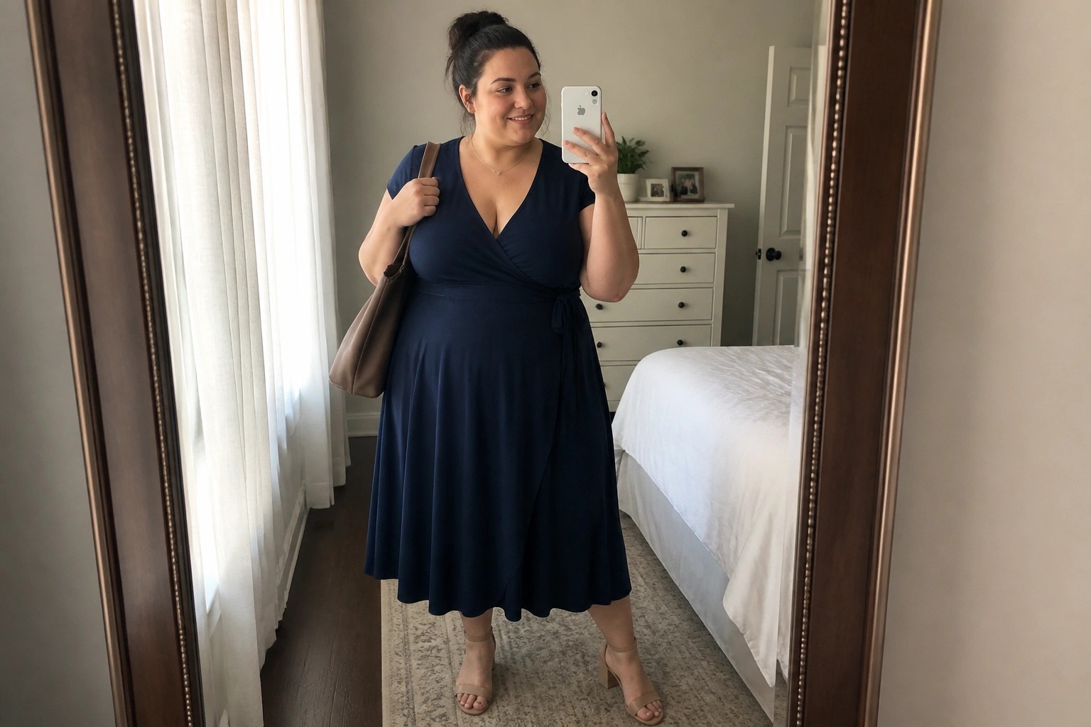 Woman in navy blue wrap dress taking mirror selfie in bedroom