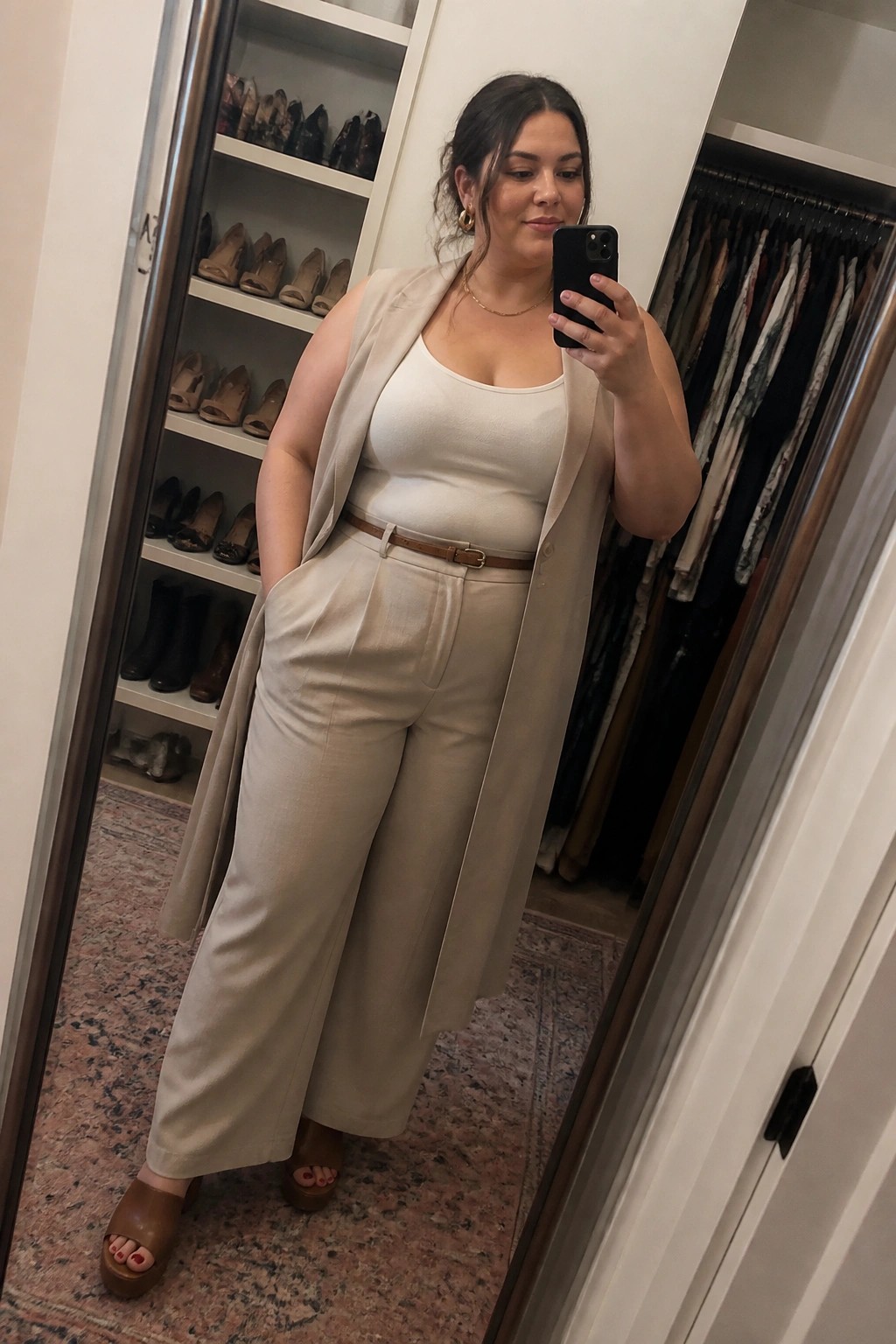 Woman in beige vest and wide pants taking mirror selfie in closet