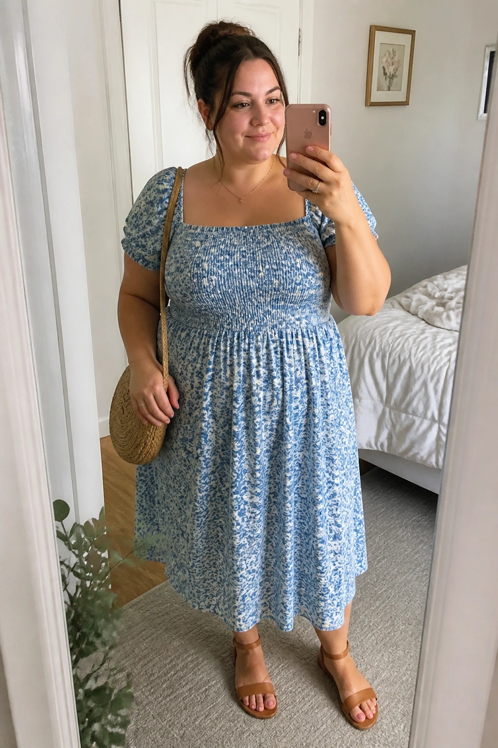 Woman in blue floral smocked midi dress taking mirror selfie with straw bag.