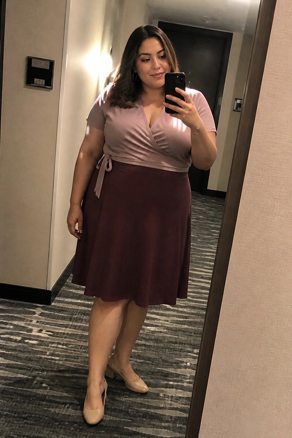 plus size woman wearing dusty rose wrap top tied at the waist with burgundy A line skirt and beige block heel pumps taking a mirror selfie