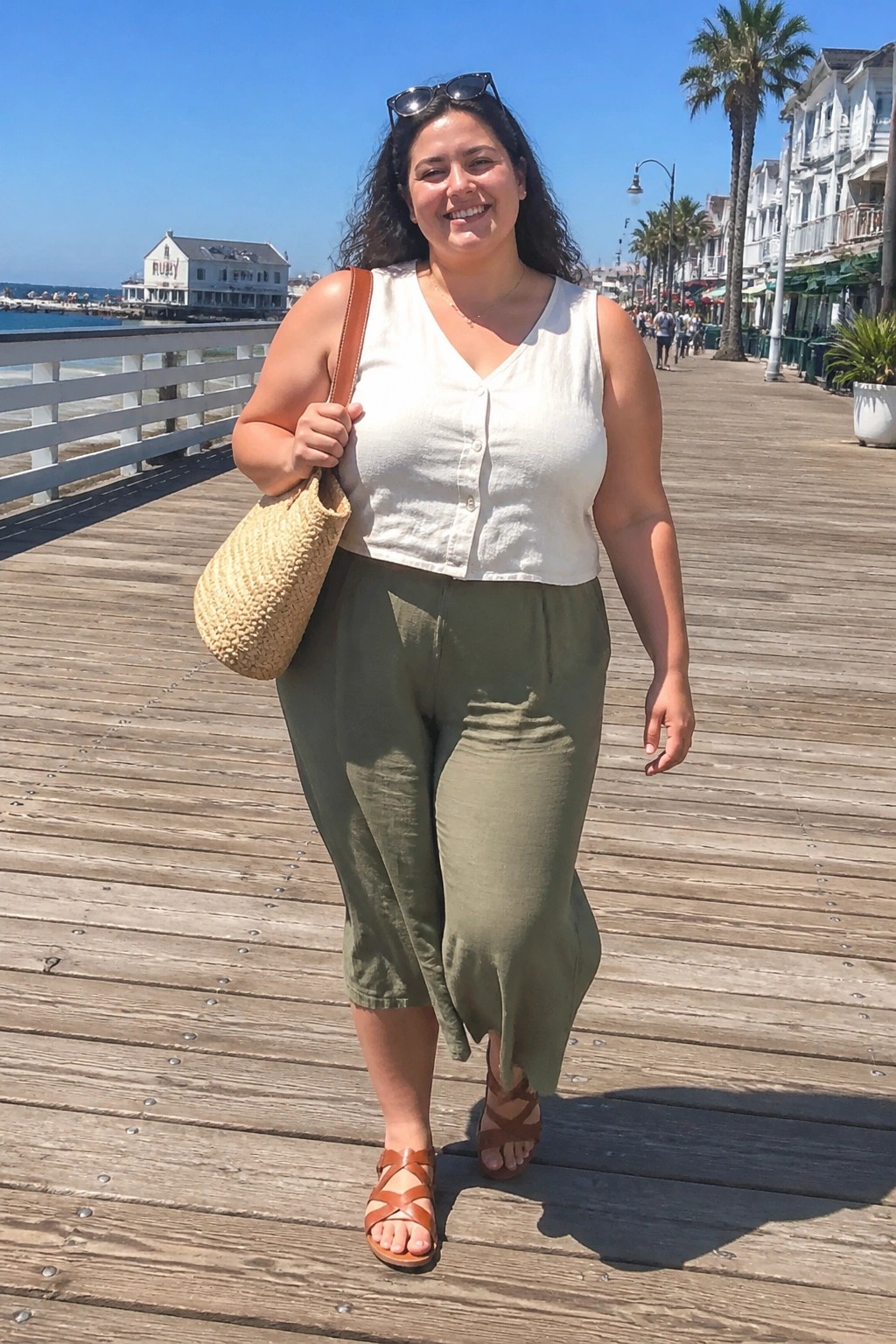 Smiling woman with straw bag on sunny boardwalk in white top and green pants