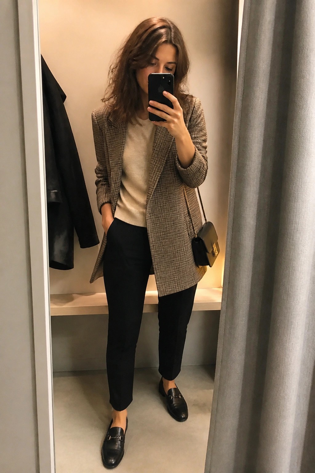 Woman taking mirror selfie in plaid blazer, beige sweater, and black pants