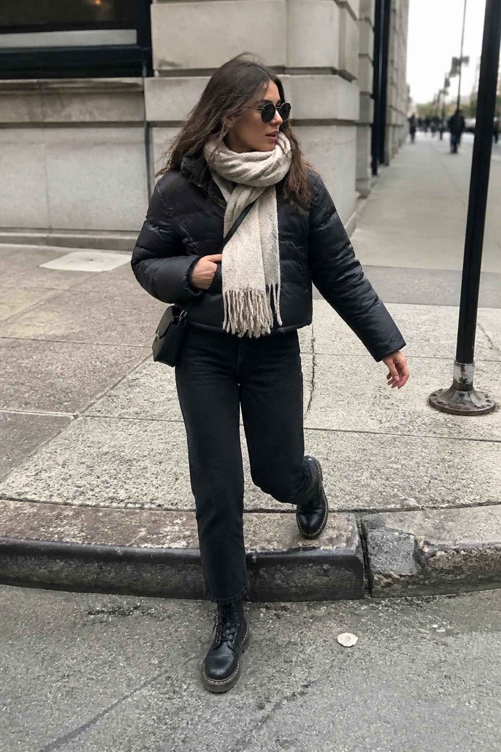 Woman in black puffer jacket and beige scarf on city sidewalk