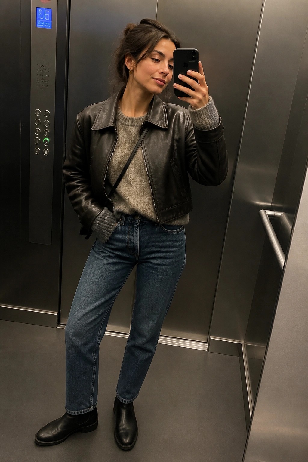 Woman in black leather jacket taking selfie inside metallic elevator.