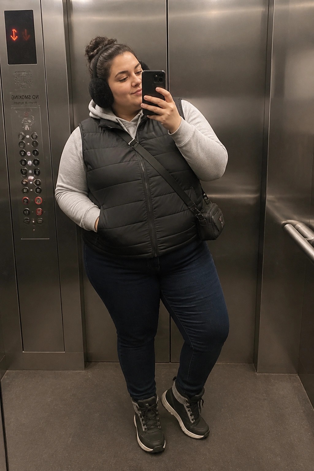 Woman in black puffer vest taking selfie in stainless steel elevator