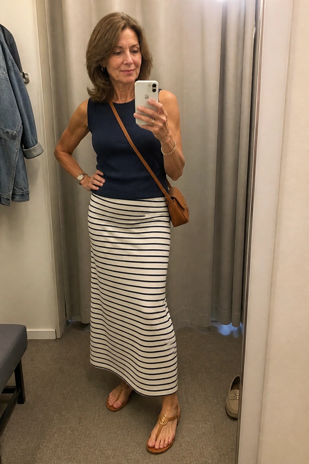 Woman in navy top and striped skirt taking mirror selfie in fitting room