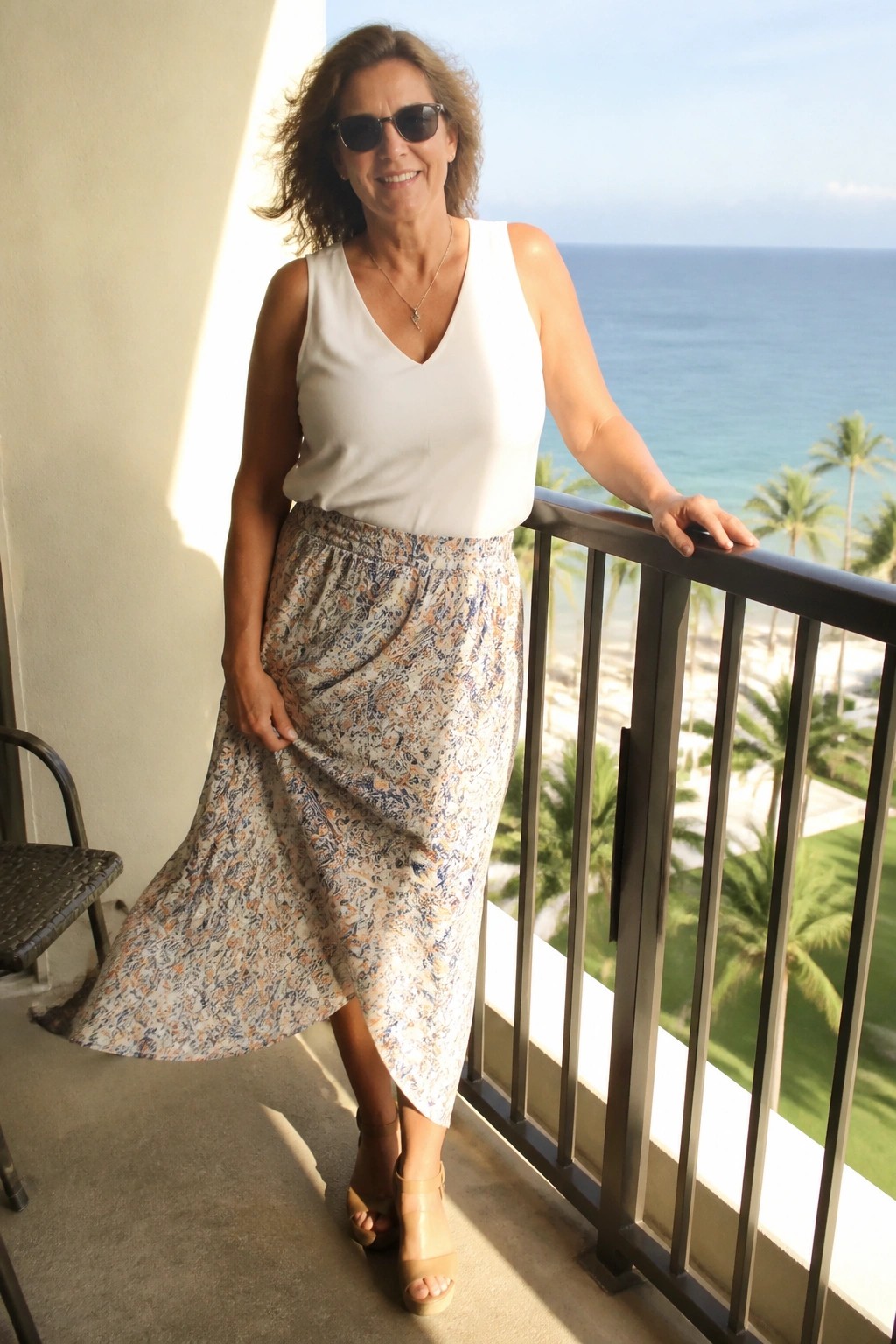 Woman in white top and floral skirt on sunny ocean-view balcony with palm trees