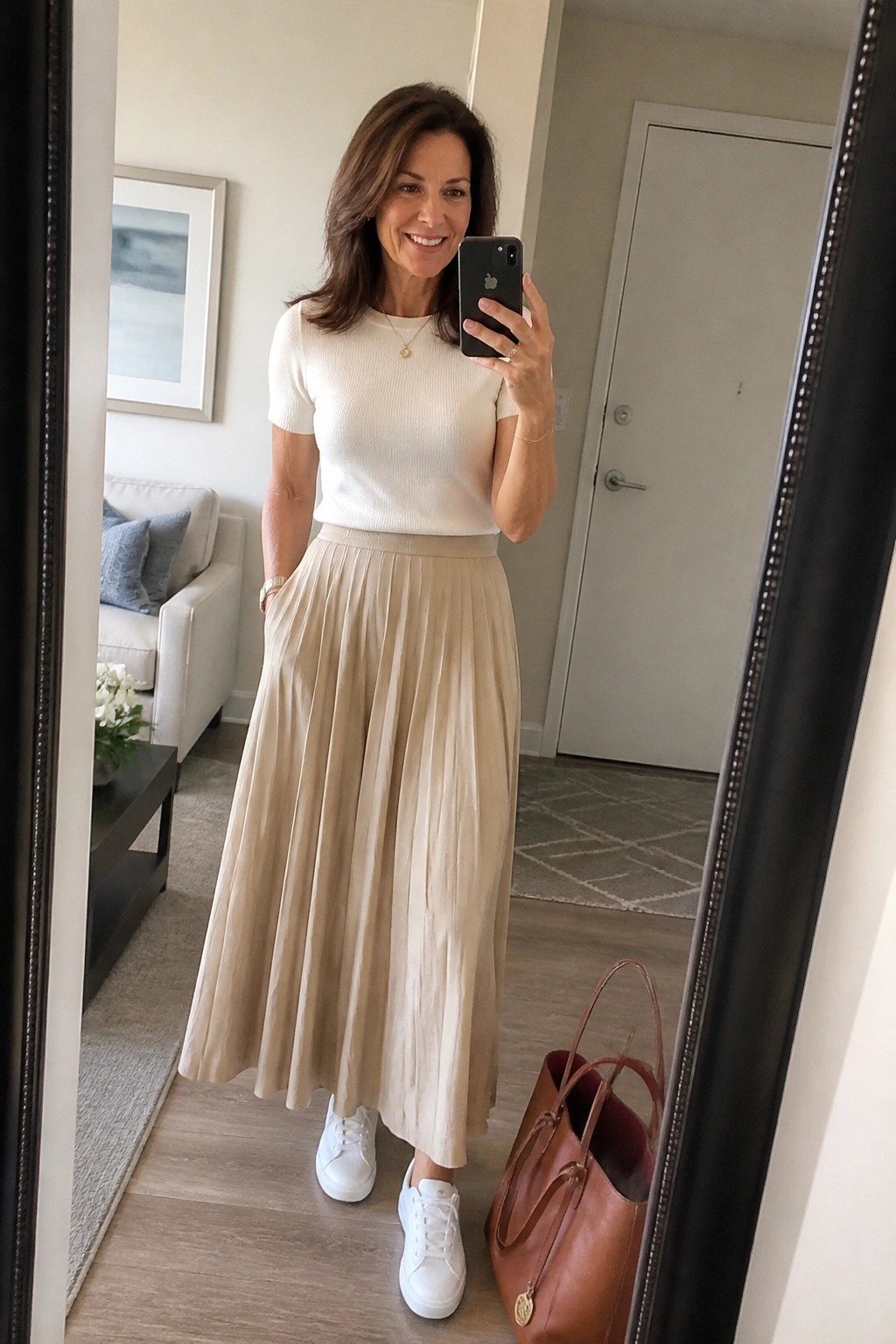 Woman in white top and beige pleated skirt taking mirror selfie wearing sneakers