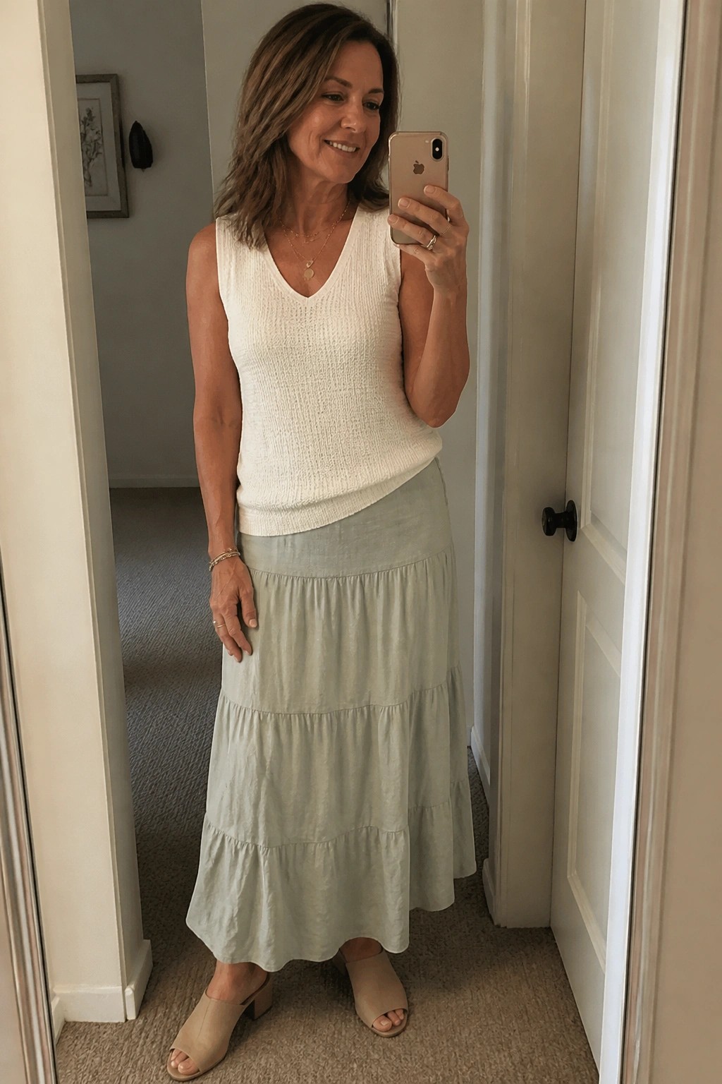 Woman taking mirror selfie in white knit top and tiered sage green skirt