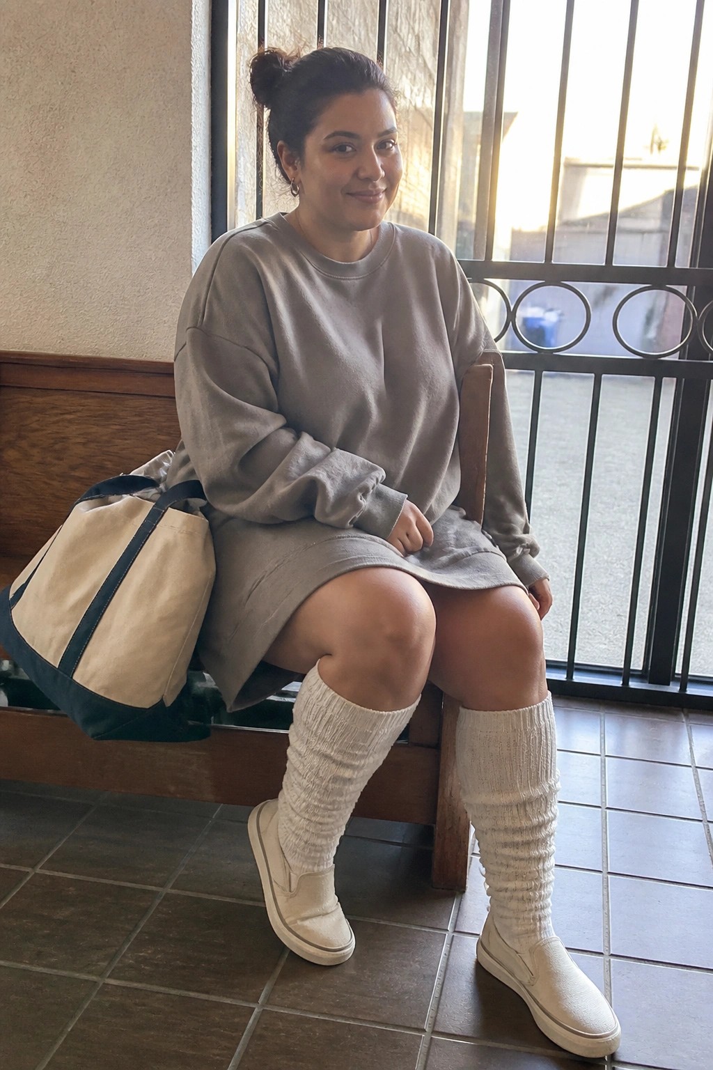 Woman in gray sweatshirt and skirt with white socks and tote bag on bench