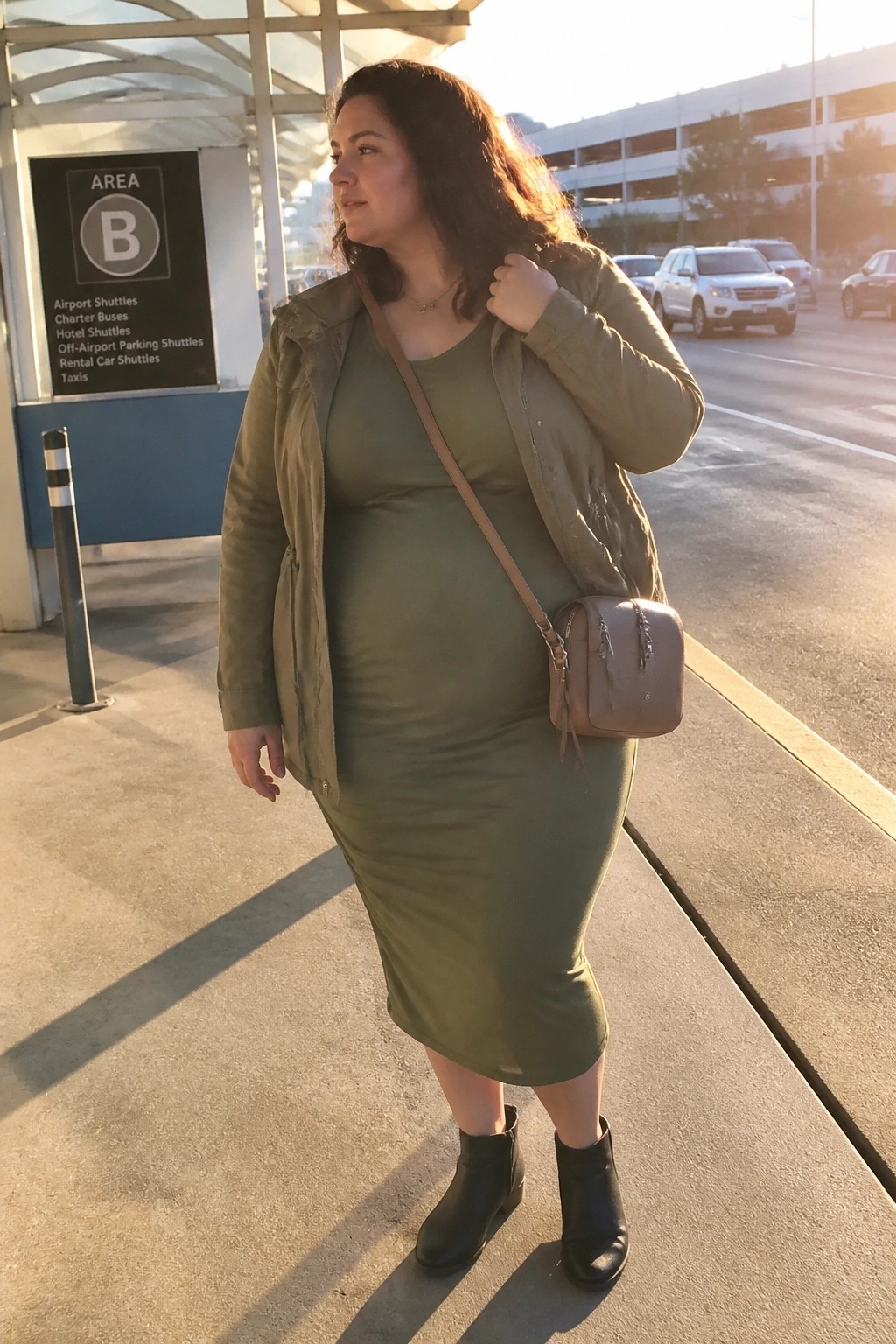Woman in olive green dress and jacket with black boots near shuttle sign
