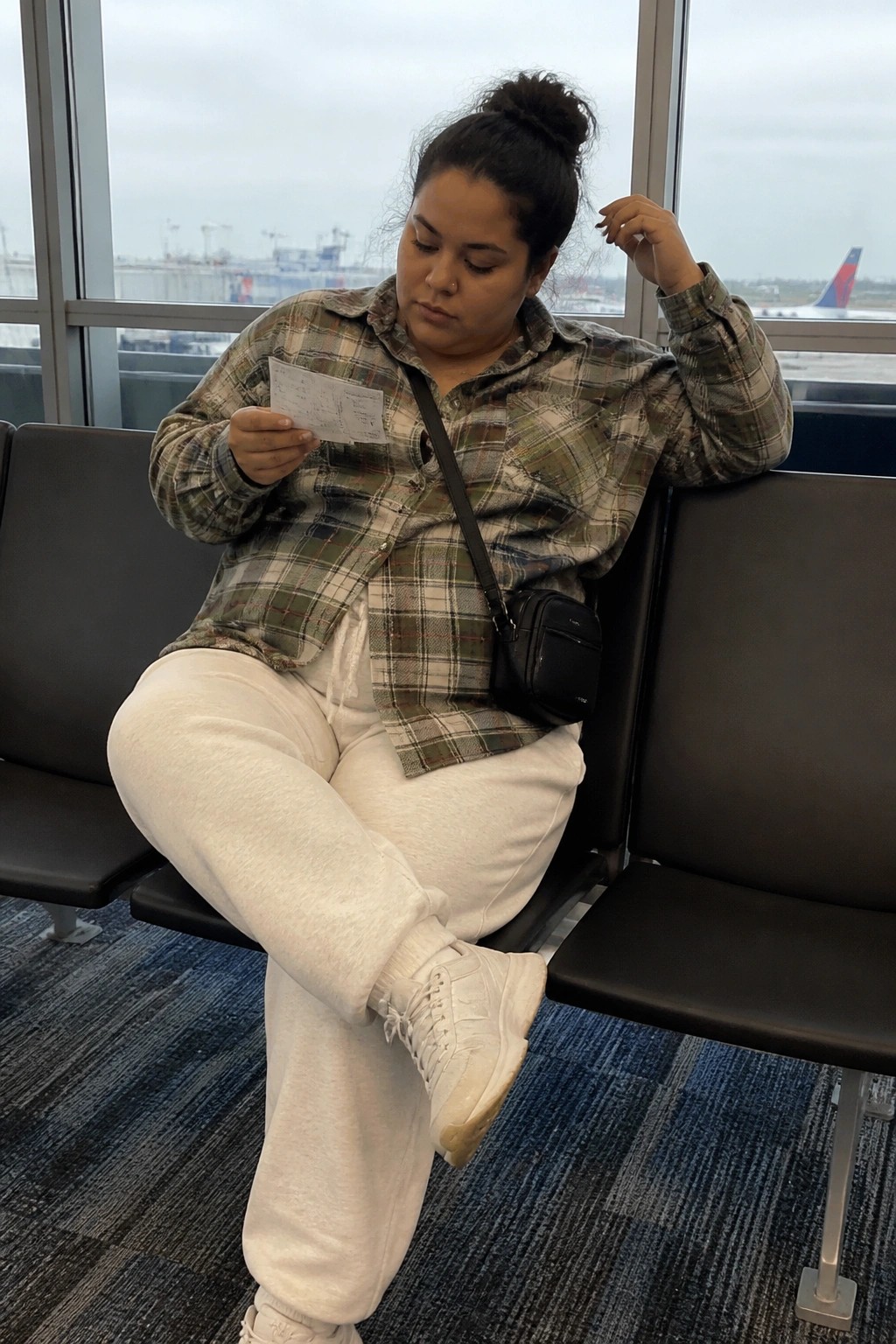 Woman in plaid shirt and white sweats reviews document at airport gate