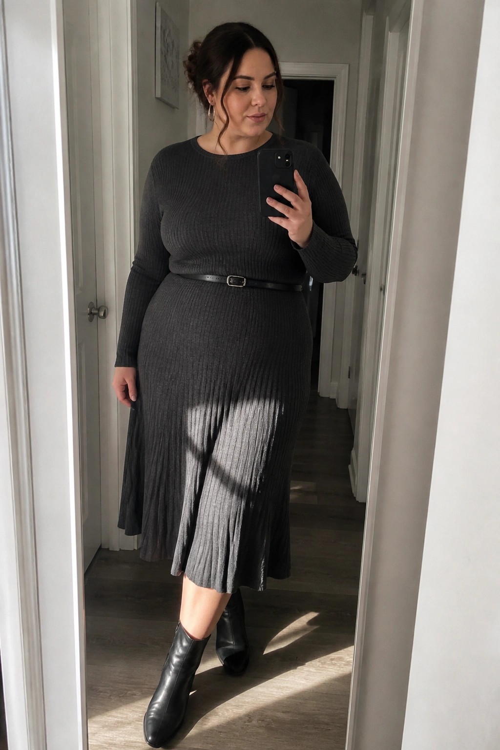 Woman in dark gray ribbed midi dress with belt taking mirror selfie in hallway