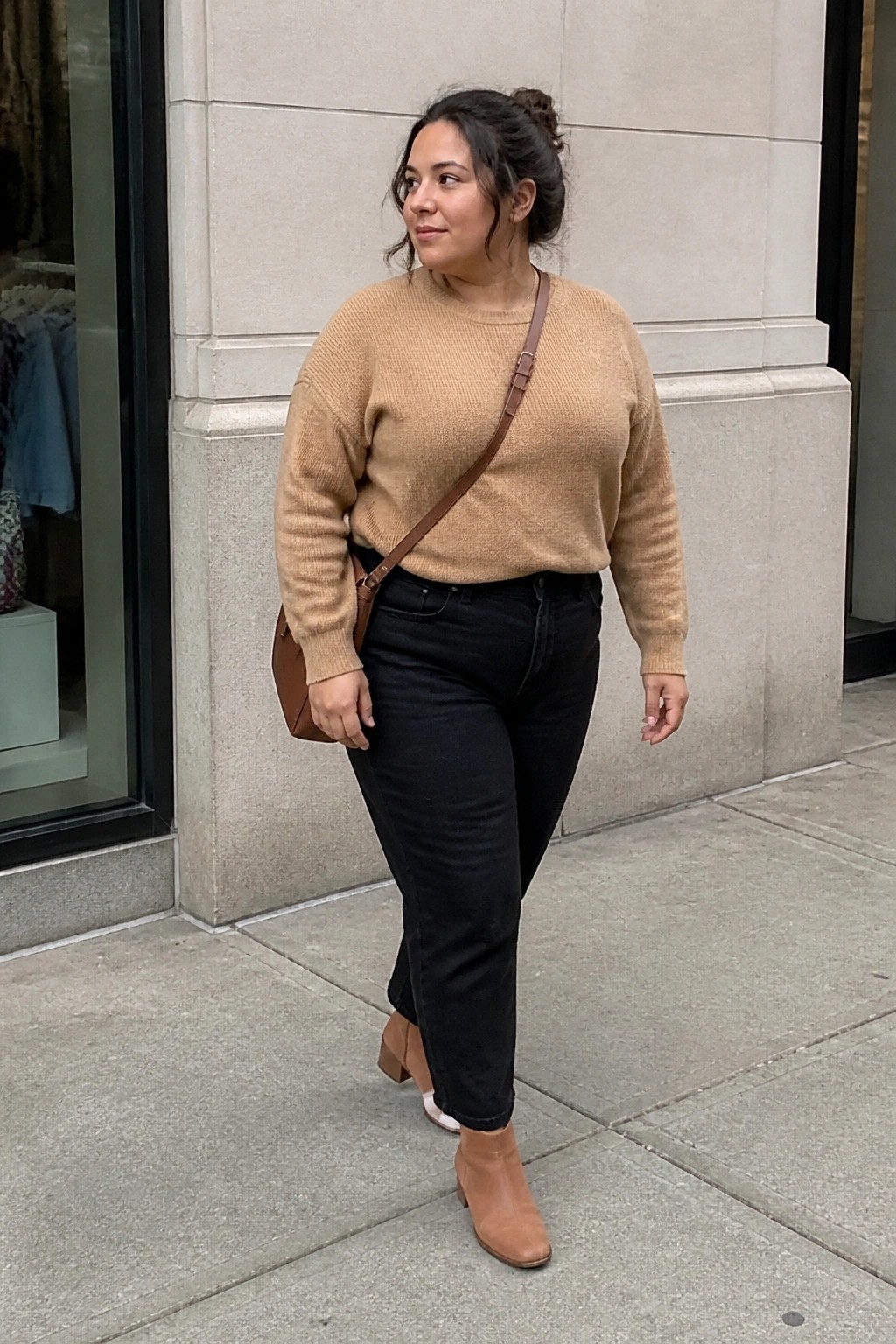 Woman in beige sweater and black jeans walking on city sidewalk with brown bag