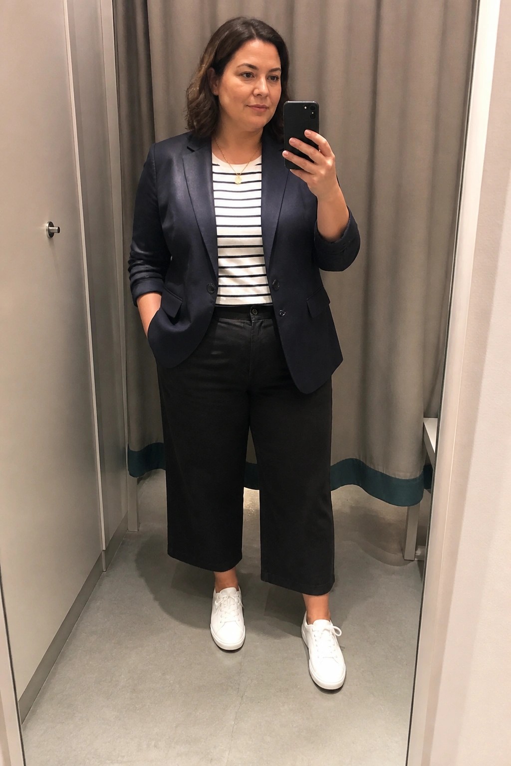 Woman in navy blazer and striped top taking mirror selfie in black pants