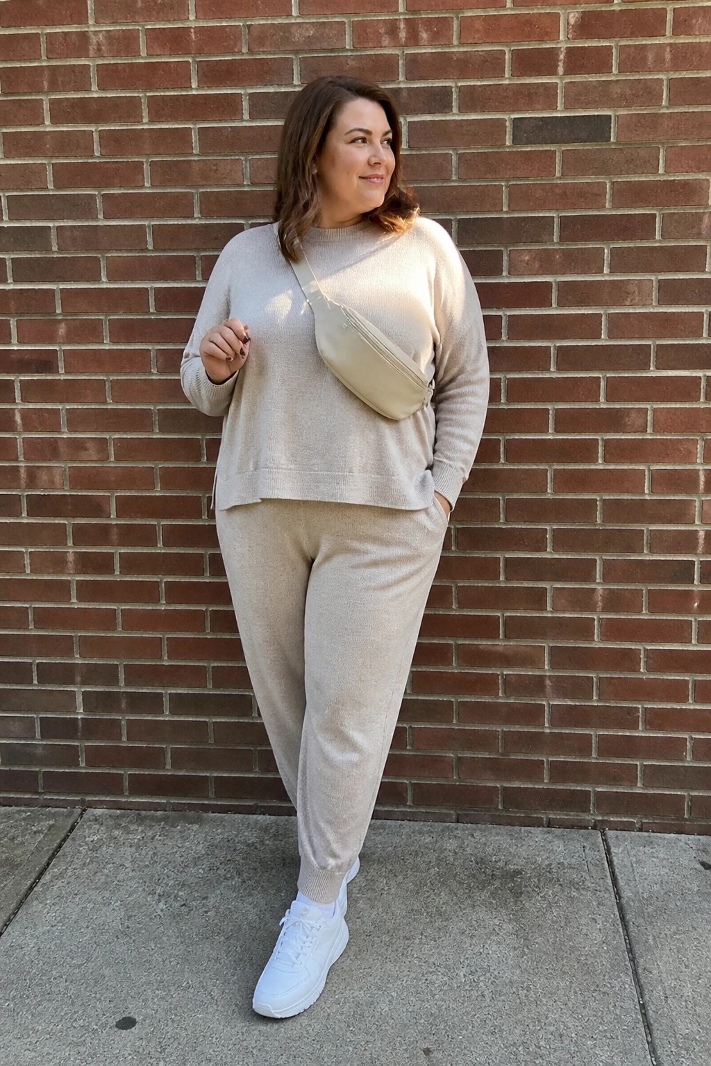 Woman in beige loungewear set with crossbody bag against red brick wall
