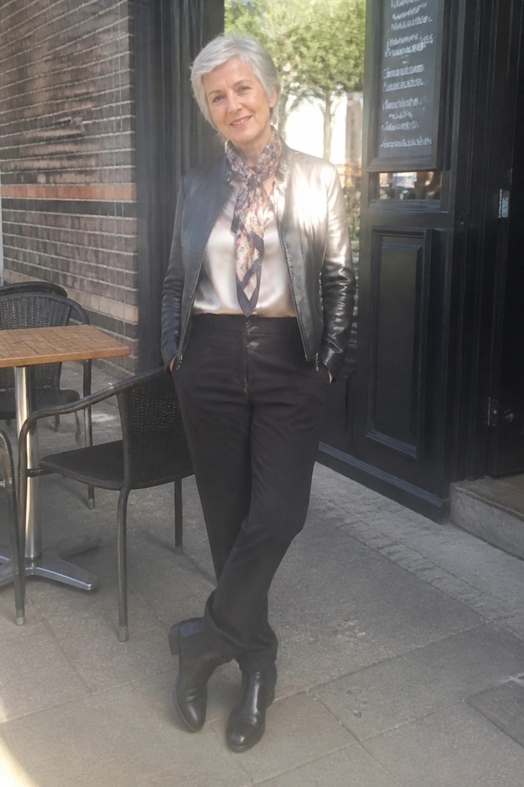 Stylish older woman in metallic jacket and scarf outside cafe entrance