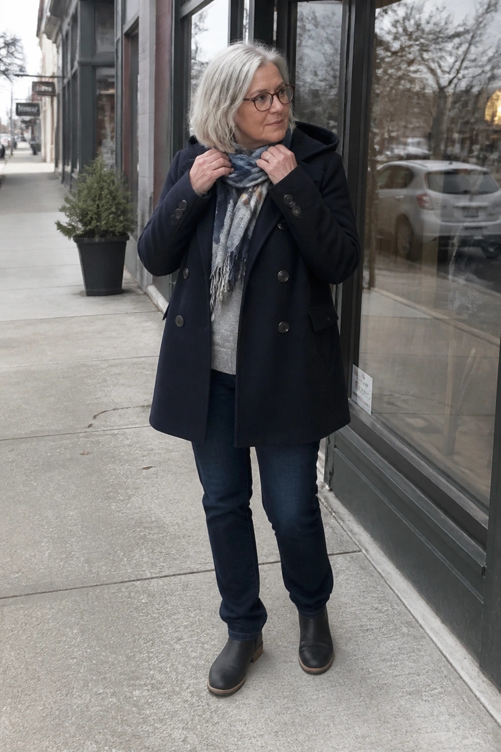 Woman with gray hair in navy coat adjusting scarf on sidewalk