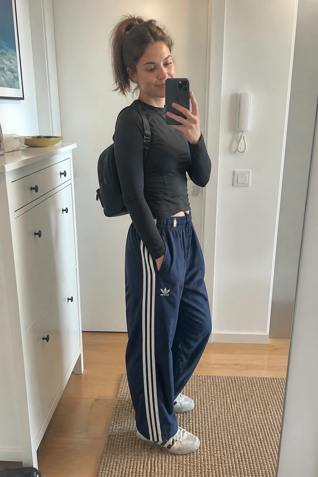 Woman in black crop top and navy Adidas track pants taking mirror selfie