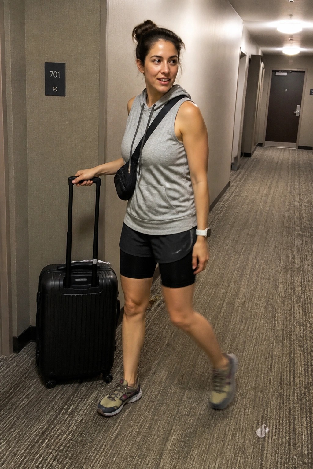 Woman in gray hoodie pulling black suitcase in hotel hallway near room 701