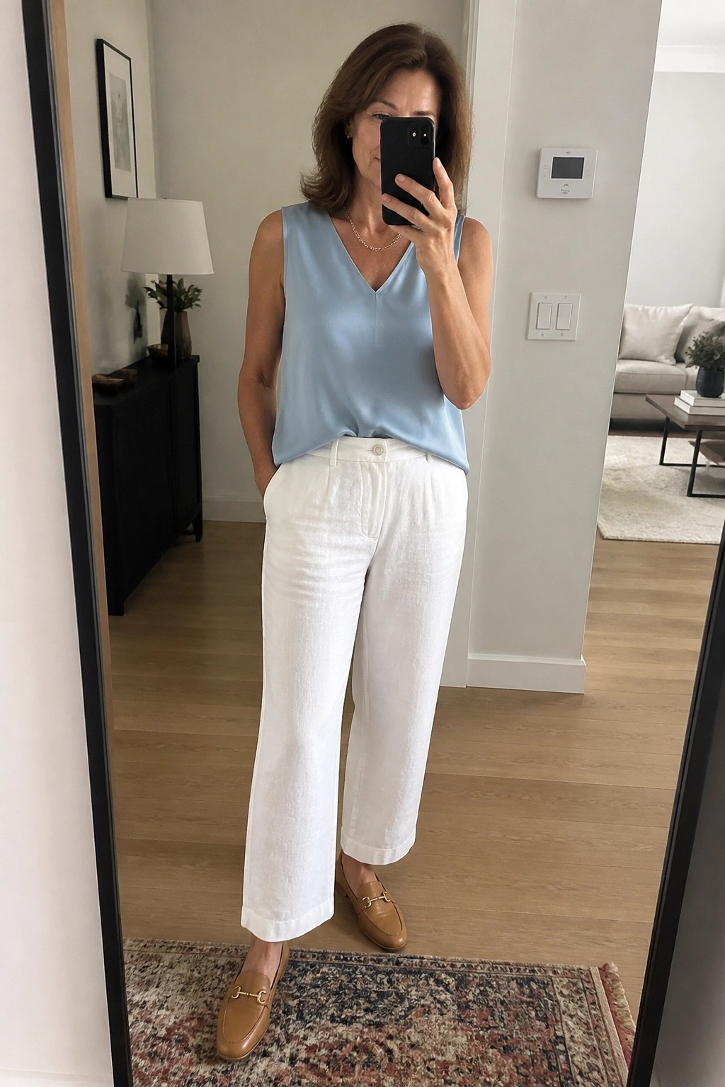 Woman wearing a light blue sleeveless V-neck top tucked into white wide-leg pants with brown loafers in a mirror selfie.