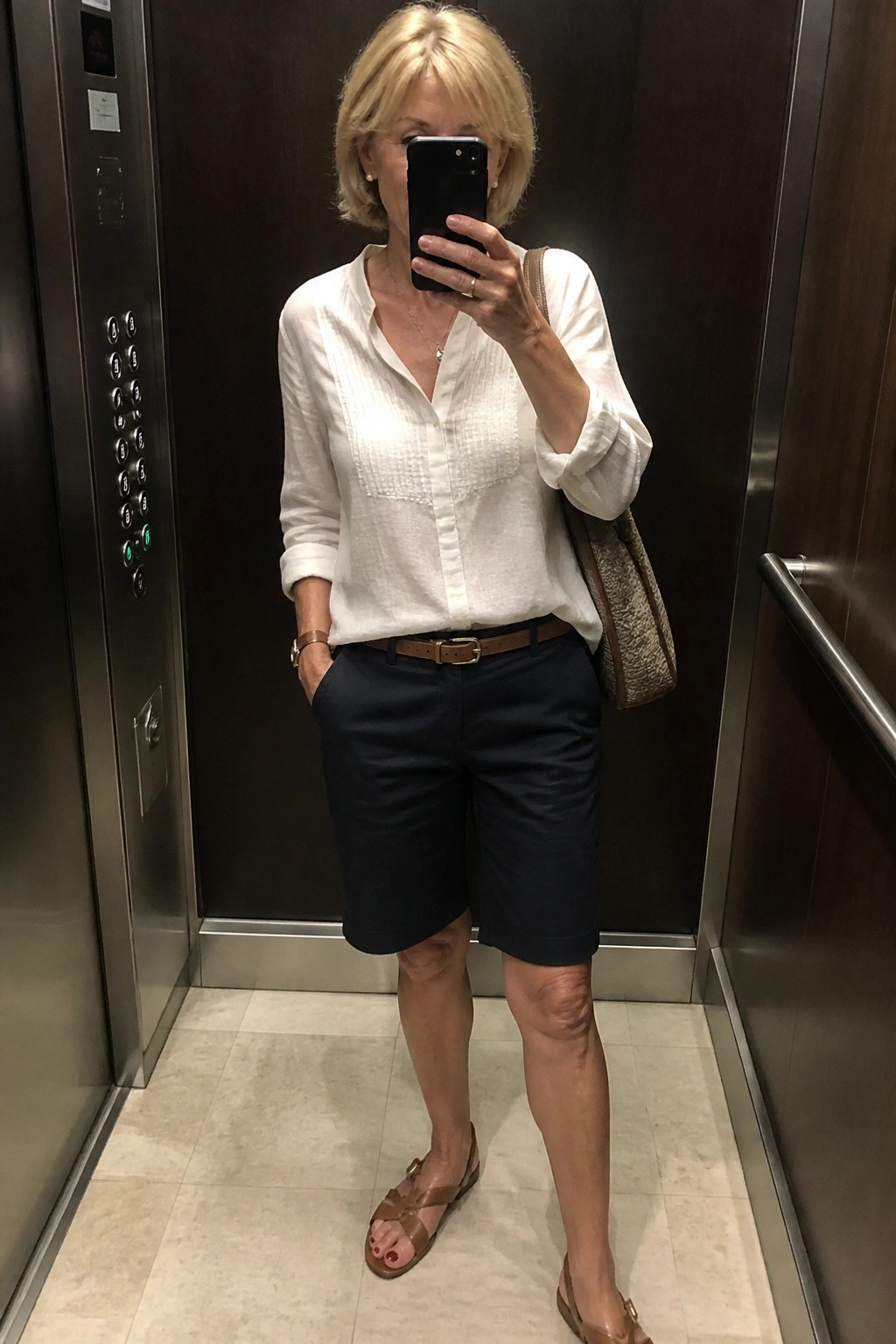 Woman taking selfie in elevator wearing white shirt, navy shorts, and sandals