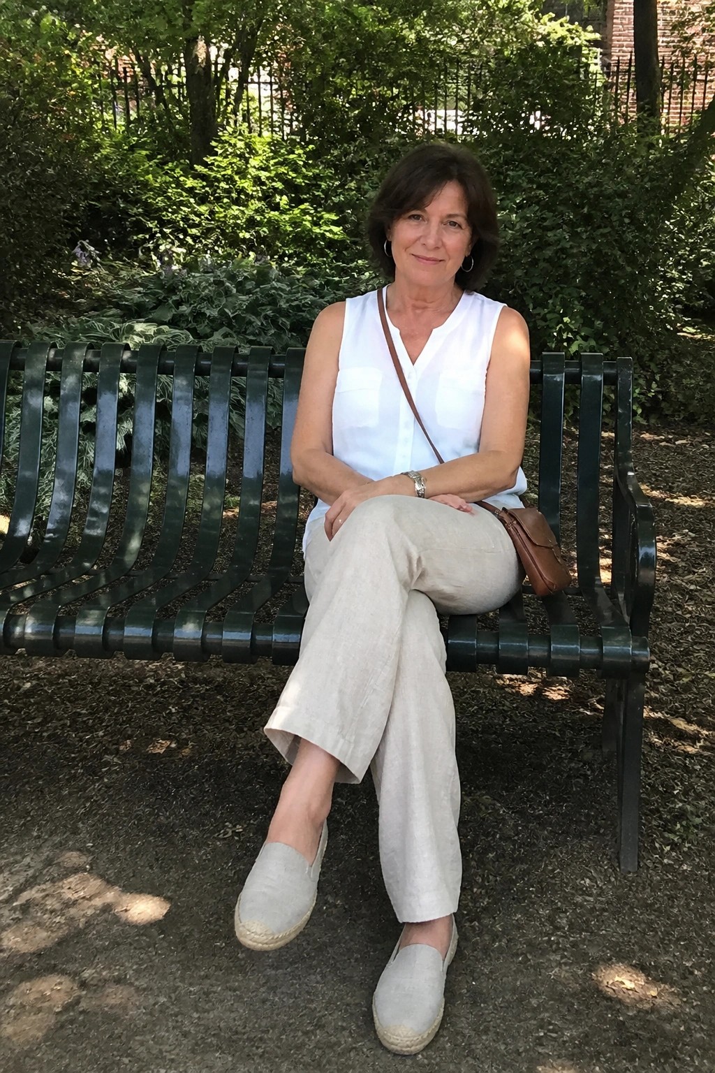 Woman in white top and beige pants seated on green park bench