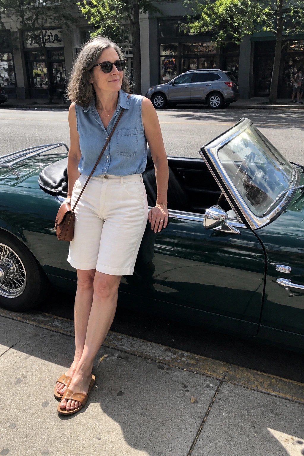 Woman in blue sleeveless shirt and white shorts beside green convertible on city street