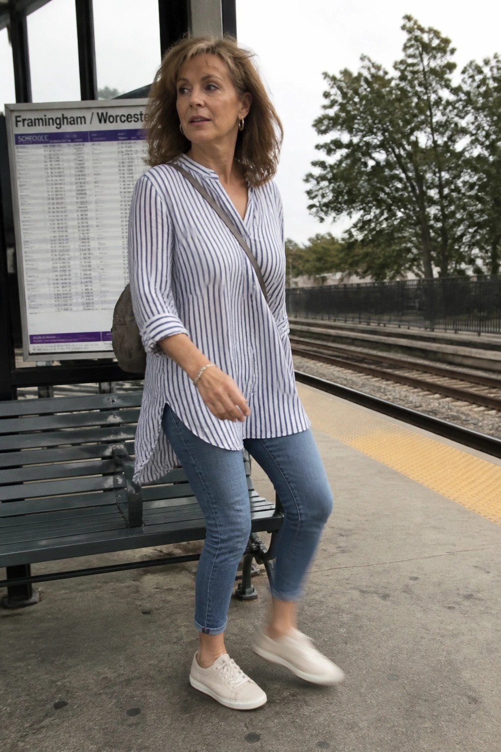 Woman in striped shirt and jeans posing at train station platform by bench