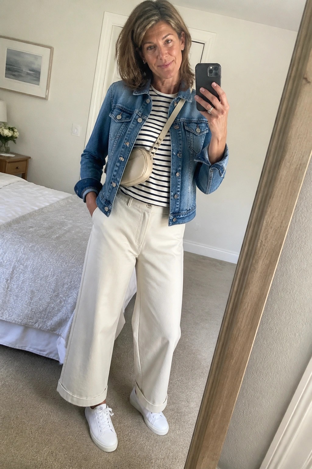 Woman in blue denim jacket and white wide-leg pants taking bedroom mirror selfie